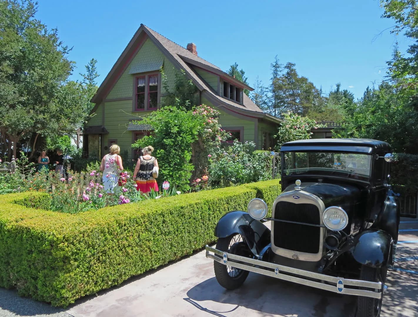 Historic green house with visitors and vintage car parked at entrance surrounded by landscaped gardens