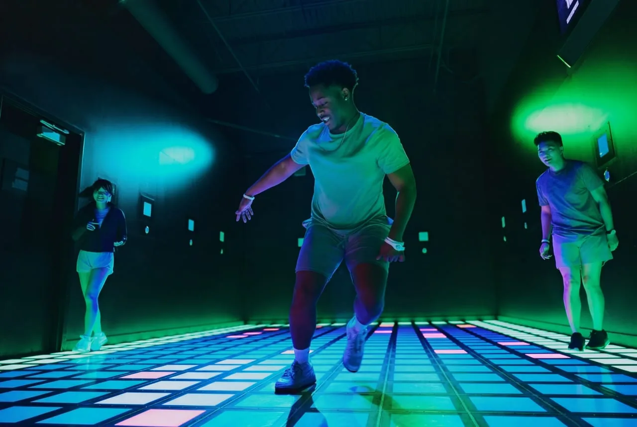 People jumping on a glowing interactive floor with neon blue and green lighting