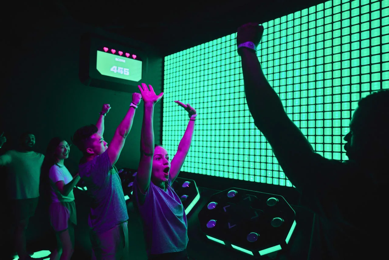 People with raised arms enjoying an interactive game under glowing green LED walls
