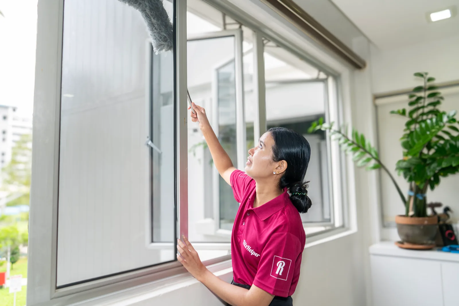Staff member cleaning a large window with professional technique in a bright residential room.