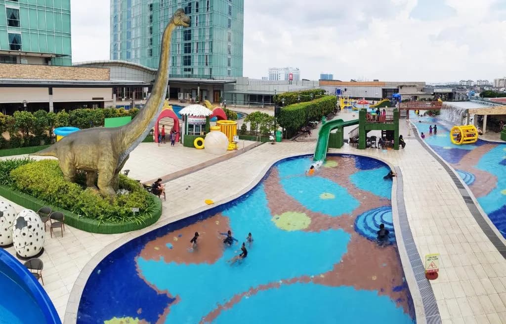 Water park with blue splash pads, green slide, dinosaur statue, and play equipment at resort