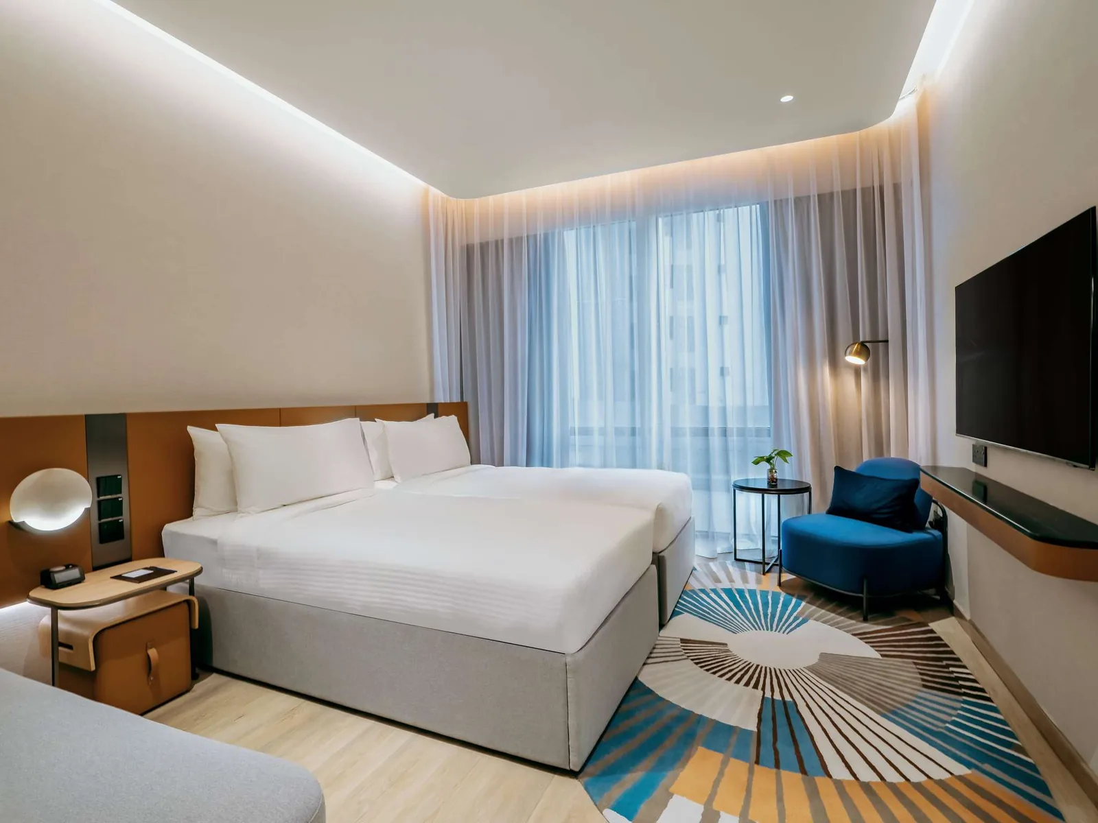 Modern hotel room with king bed, blue seating, wooden headboard, and ambient lighting