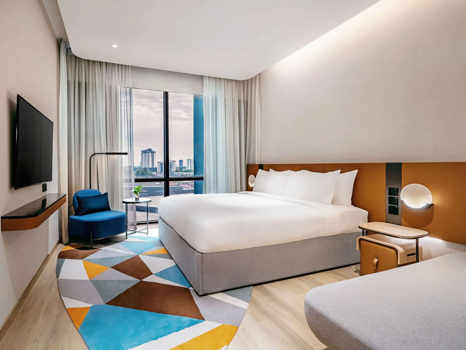 Bright modern hotel room with city view, two beds, blue accent chair, and geometric floor pattern