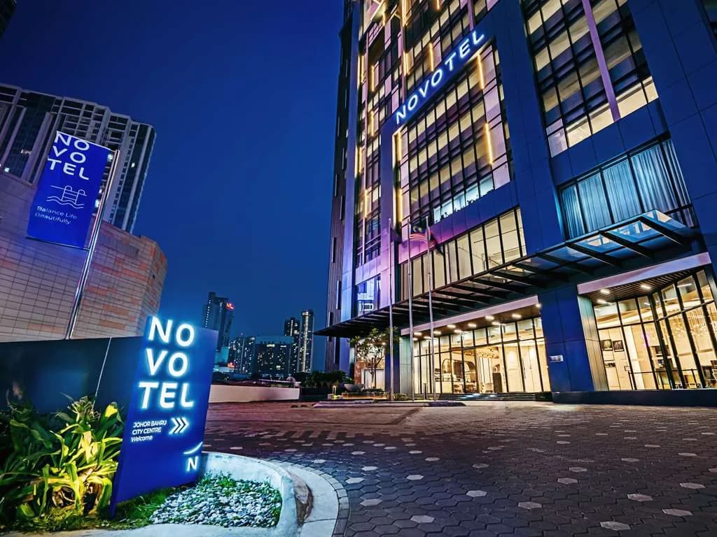 Novotel hotel building lit up at night with blue neon signage and glass entrance on paved plaza