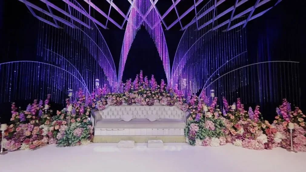 Wedding ceremony stage with pink and white floral decorations and purple lighting