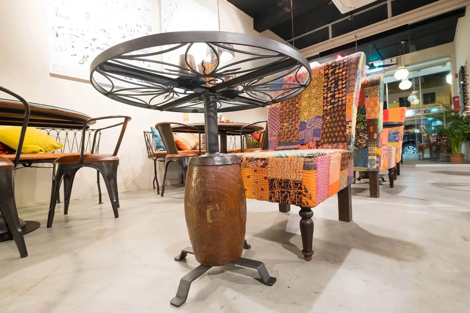 Restaurant interior with colorful patterned fabrics, wooden furniture, and unique barrel-based table design.