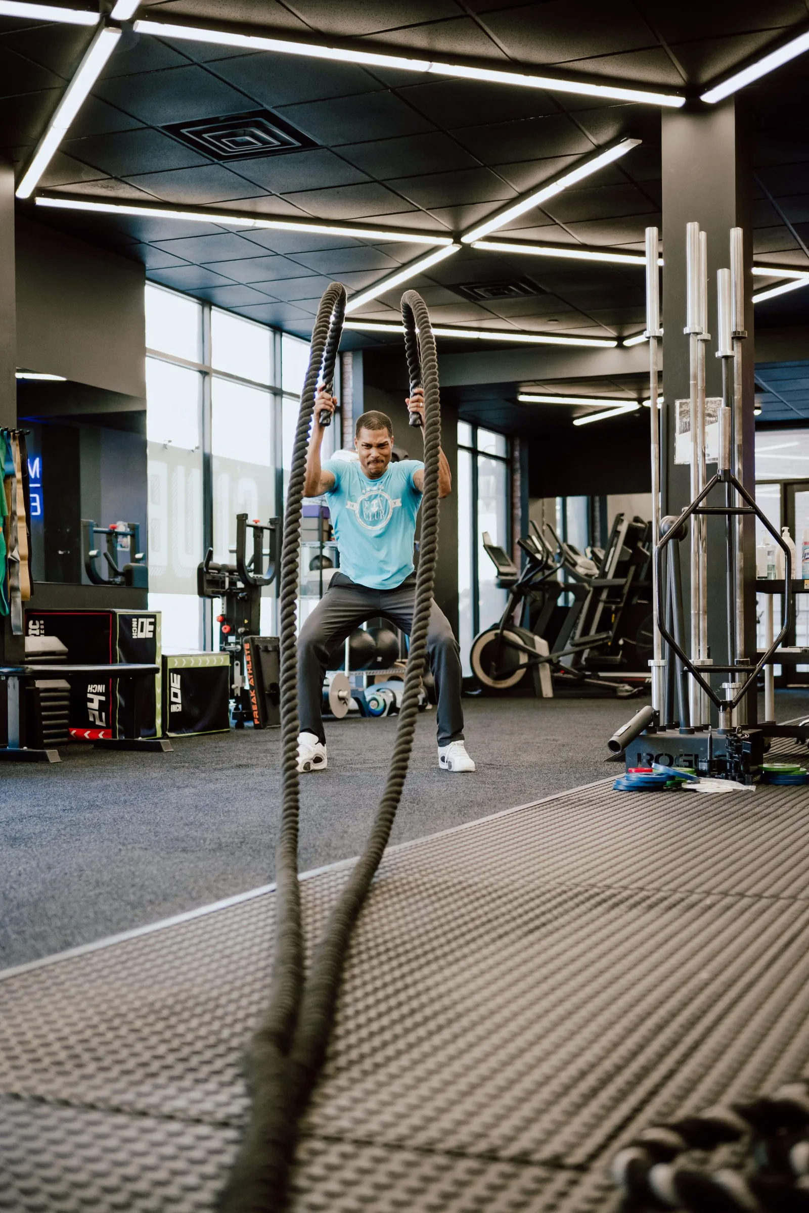 Man doing battle rope exercise in contemporary gym with modern lighting and equipment