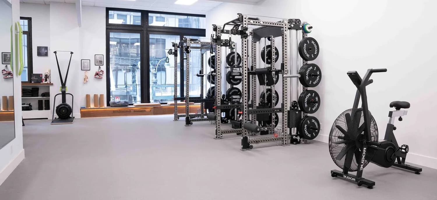 Bright physical therapy gym with weight machines, resistance racks, exercise bike, and training equipment