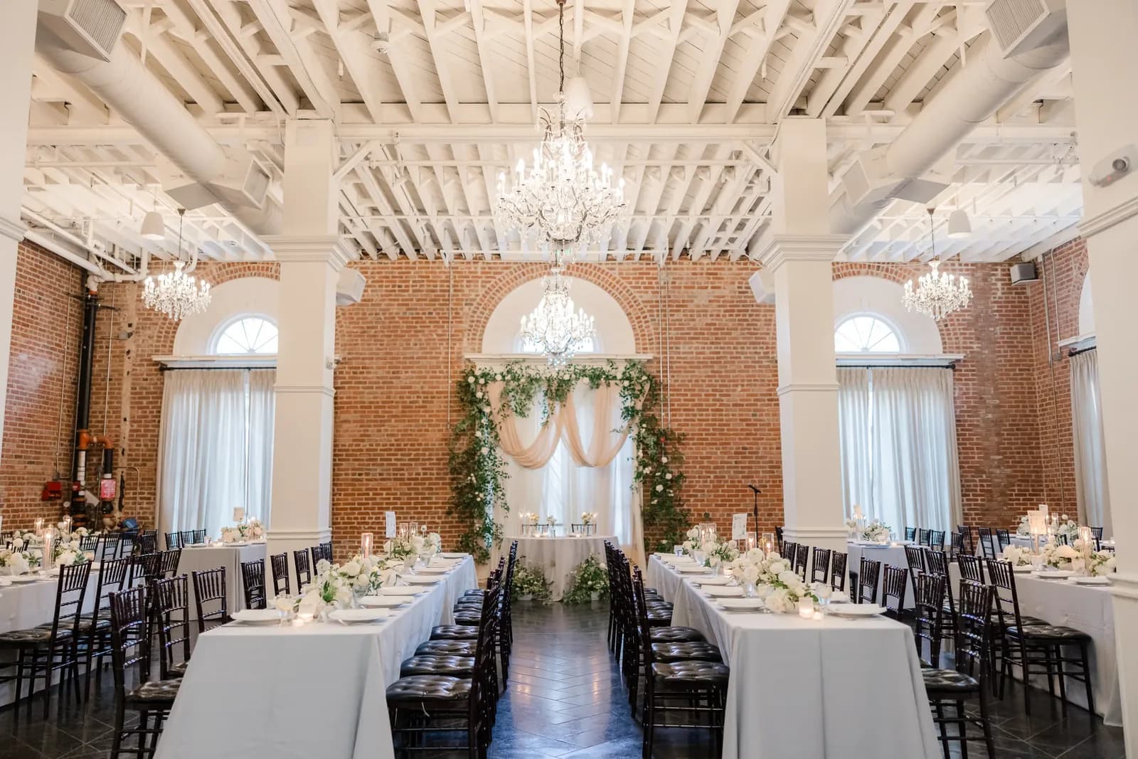 Elegant ballroom with white beamed ceiling, crystal chandeliers, brick walls, and formally set dining tables