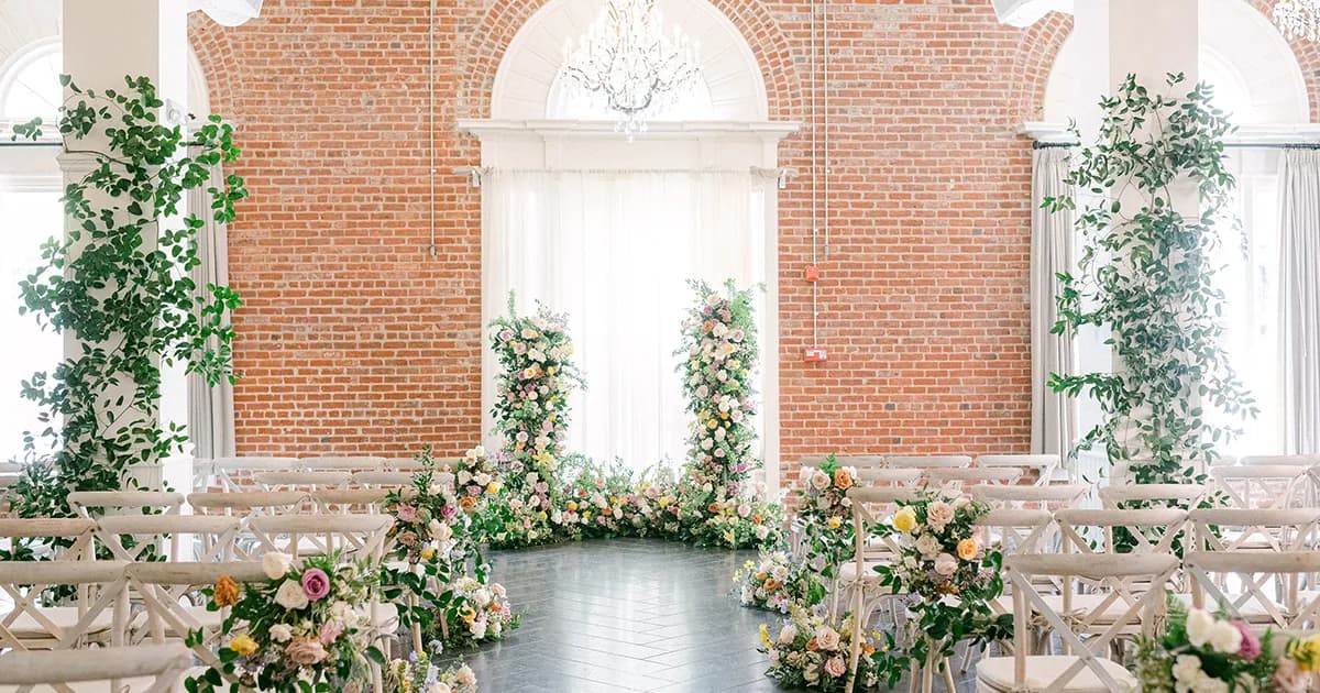 Brick event venue decorated with white chairs, floral arrangements, and greenery for a wedding ceremony