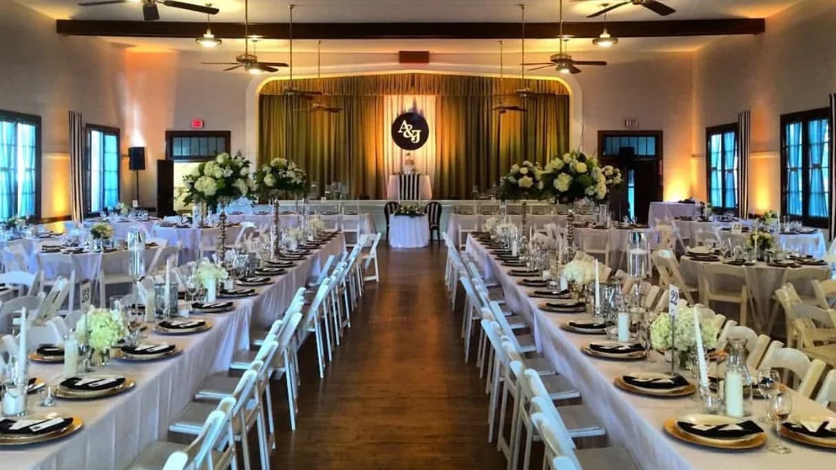 Elegant ballroom setup with long banquet tables, formal place settings, and white floral centerpieces.