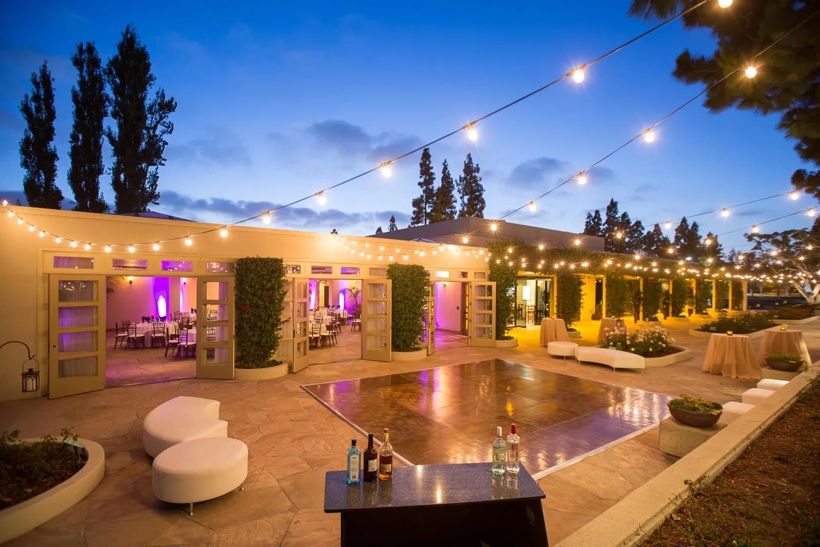 Upscale outdoor event venue with illuminated dance floor, pavilion, and string lighting at twilight