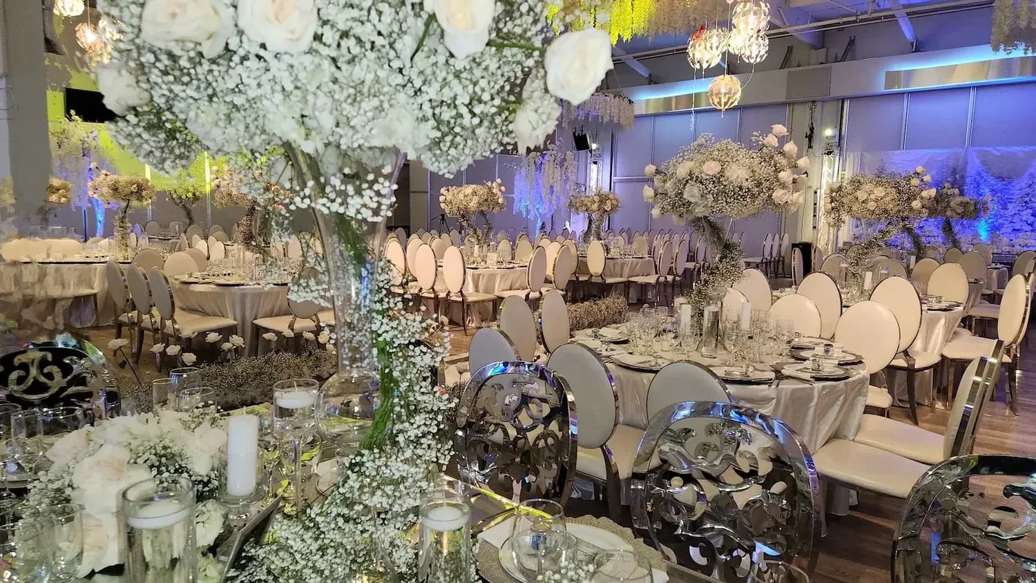 Formal event venue with white flowers, elegant table settings, and blue ambient lighting