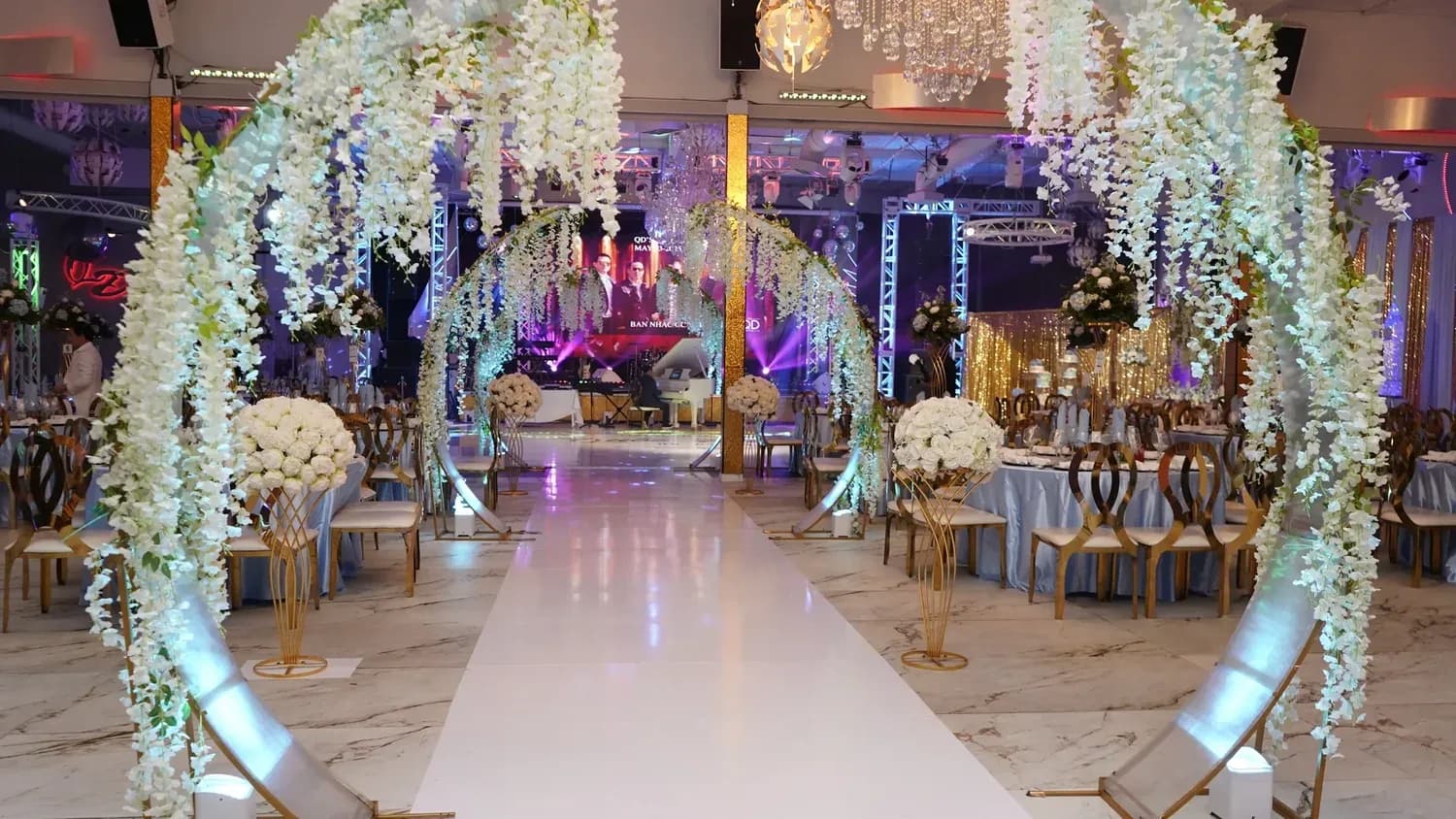 Decorated event space with white hanging flowers, gold chairs, and illuminated aisle