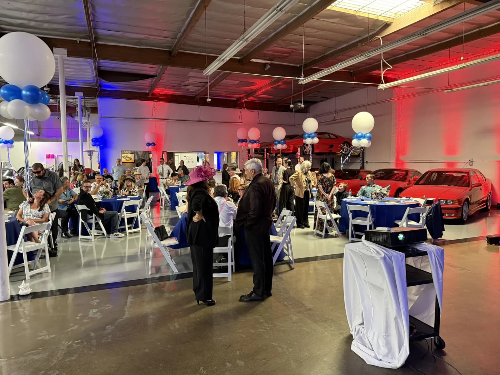 Event space with guests dining at tables, red and blue lighting, and cars displayed inside