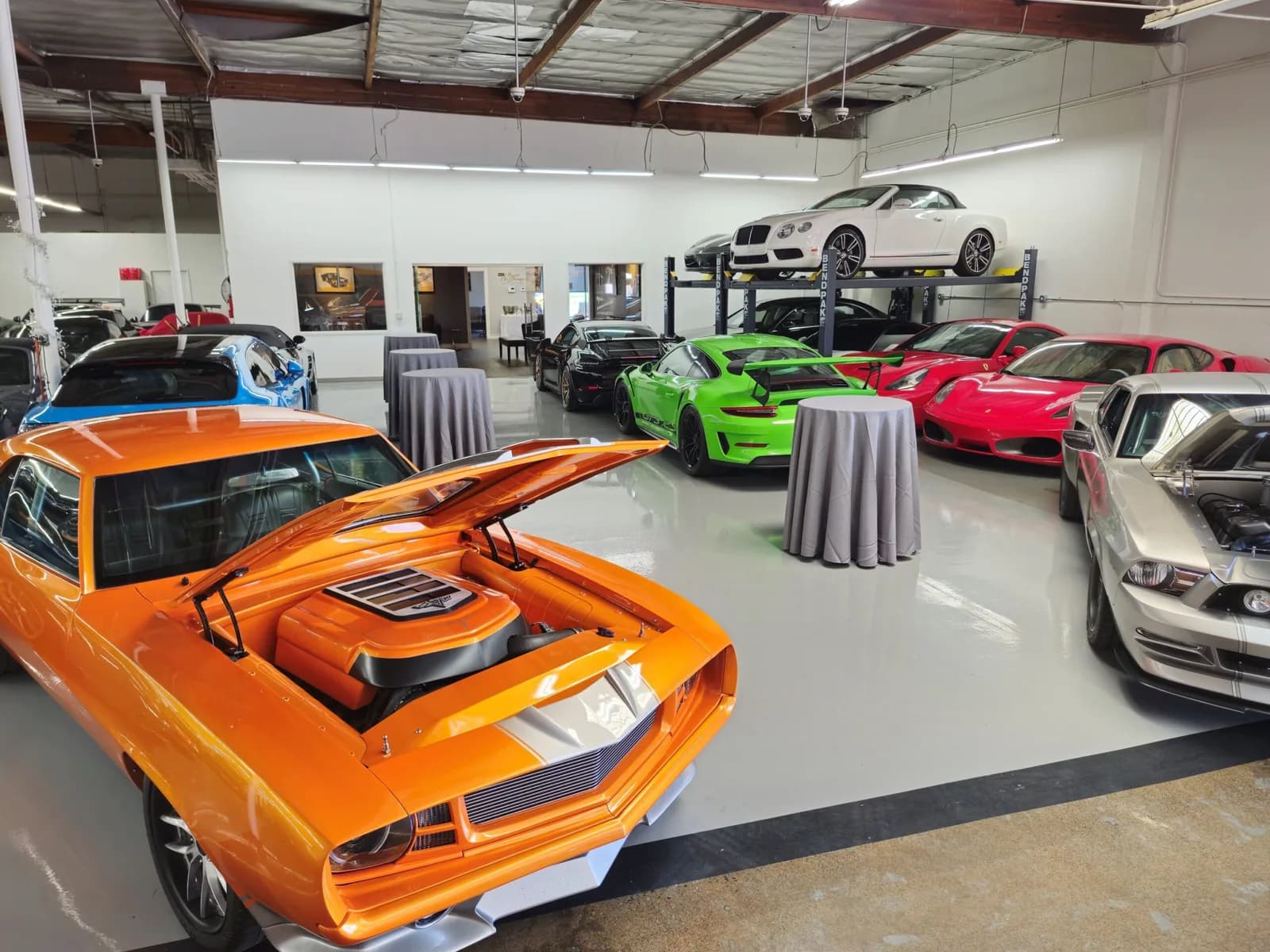 Classic and luxury cars displayed in a bright, spacious event venue with polished flooring and professional lighting