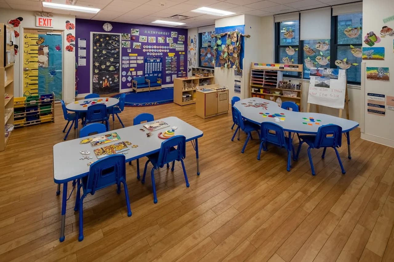 Preschool classroom with small blue chairs, activity tables, educational wall displays, and learning materials
