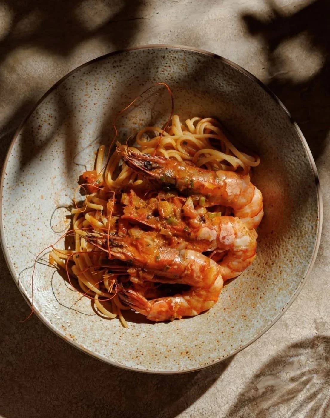 Four glazed prawns on crispy noodles in a speckled ceramic bowl