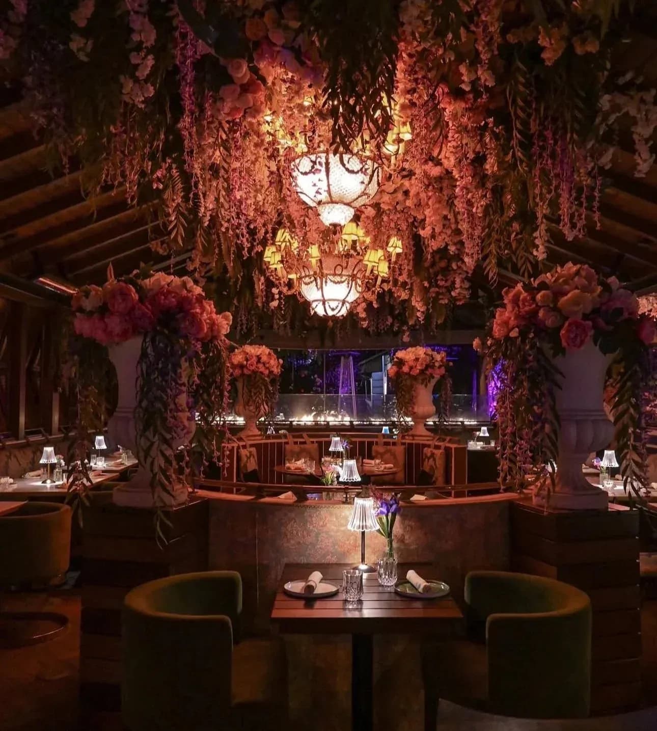 Fine dining restaurant with elaborate hanging floral arrangements, chandeliers, and table settings with city views