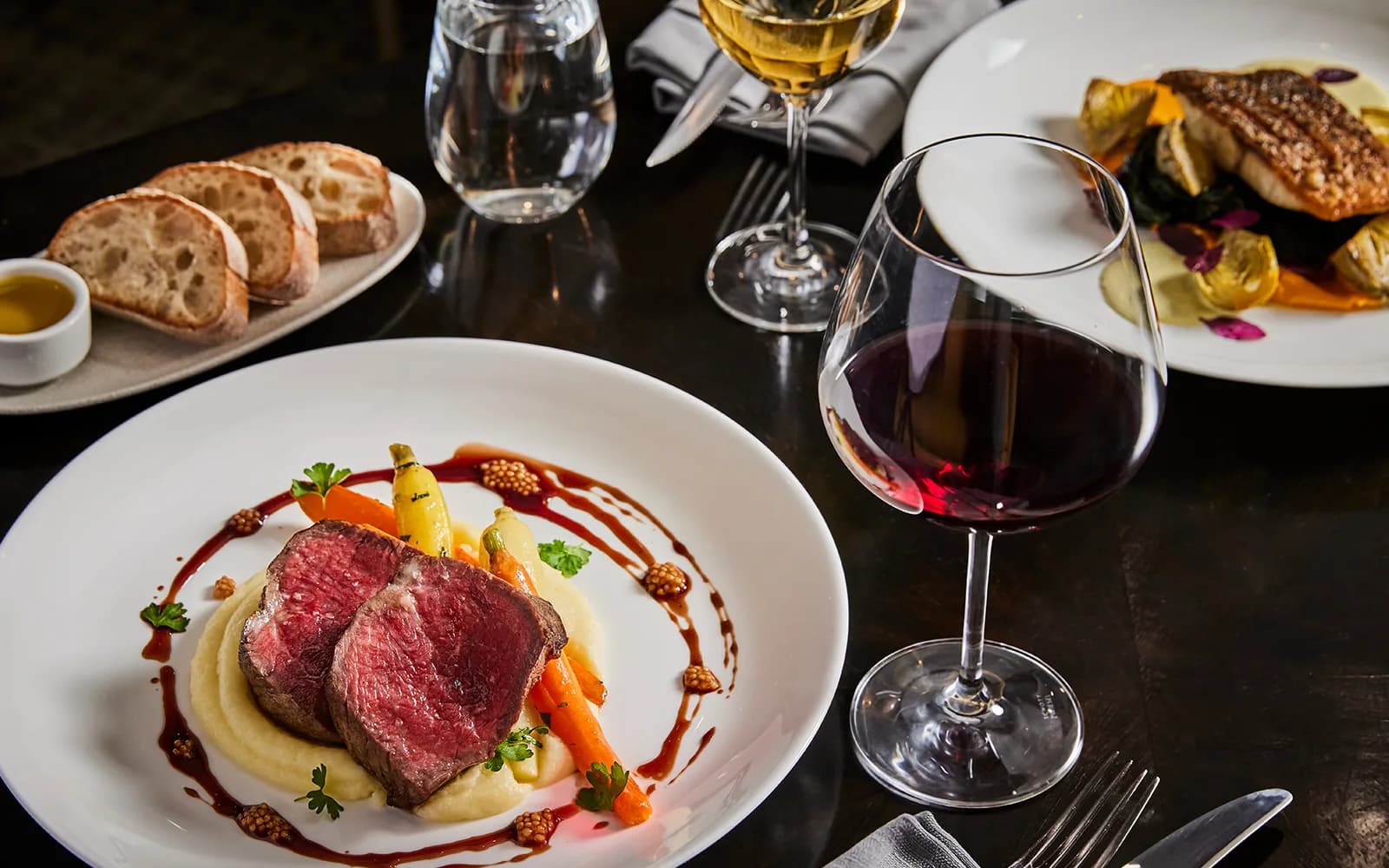 Fine dining plate with sliced duck breast, potato puree, and vegetables, paired with red wine and bread