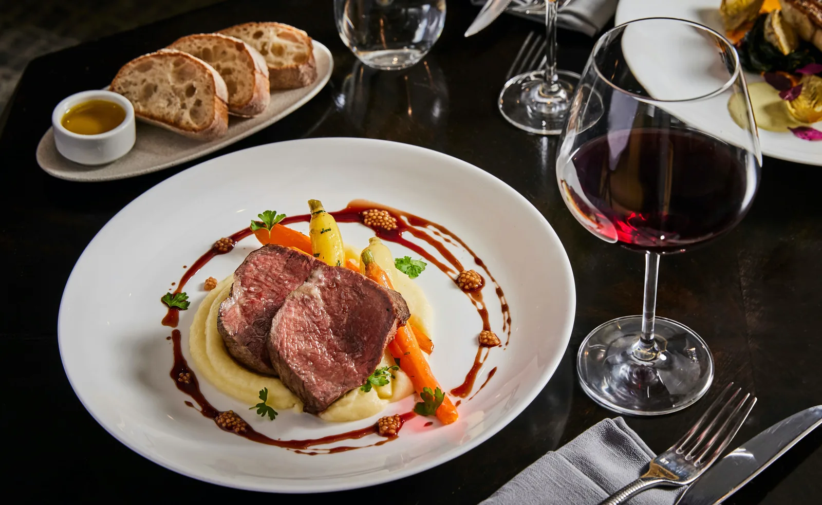 Gourmet plated duck with potato puree, vegetables, and red wine reduction at fine dining table