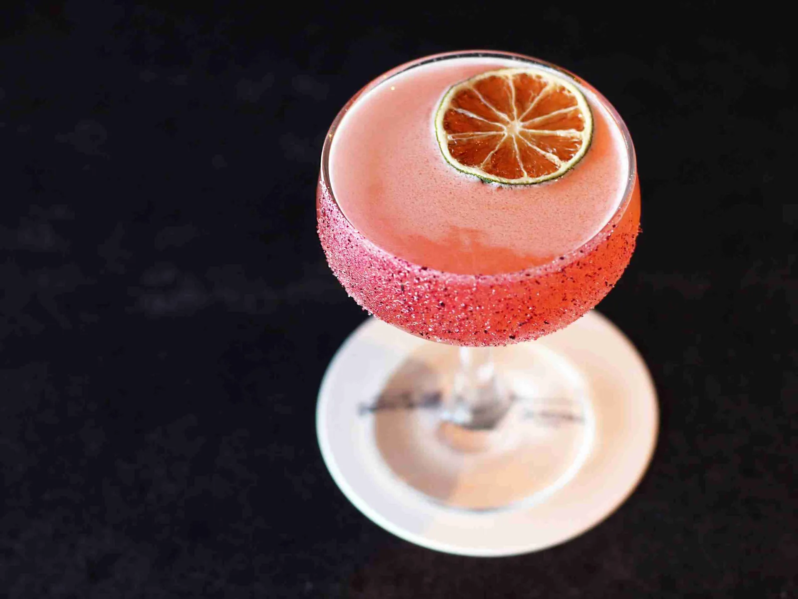 Pink cocktail with grapefruit slice garnish and sugar rim on white plate