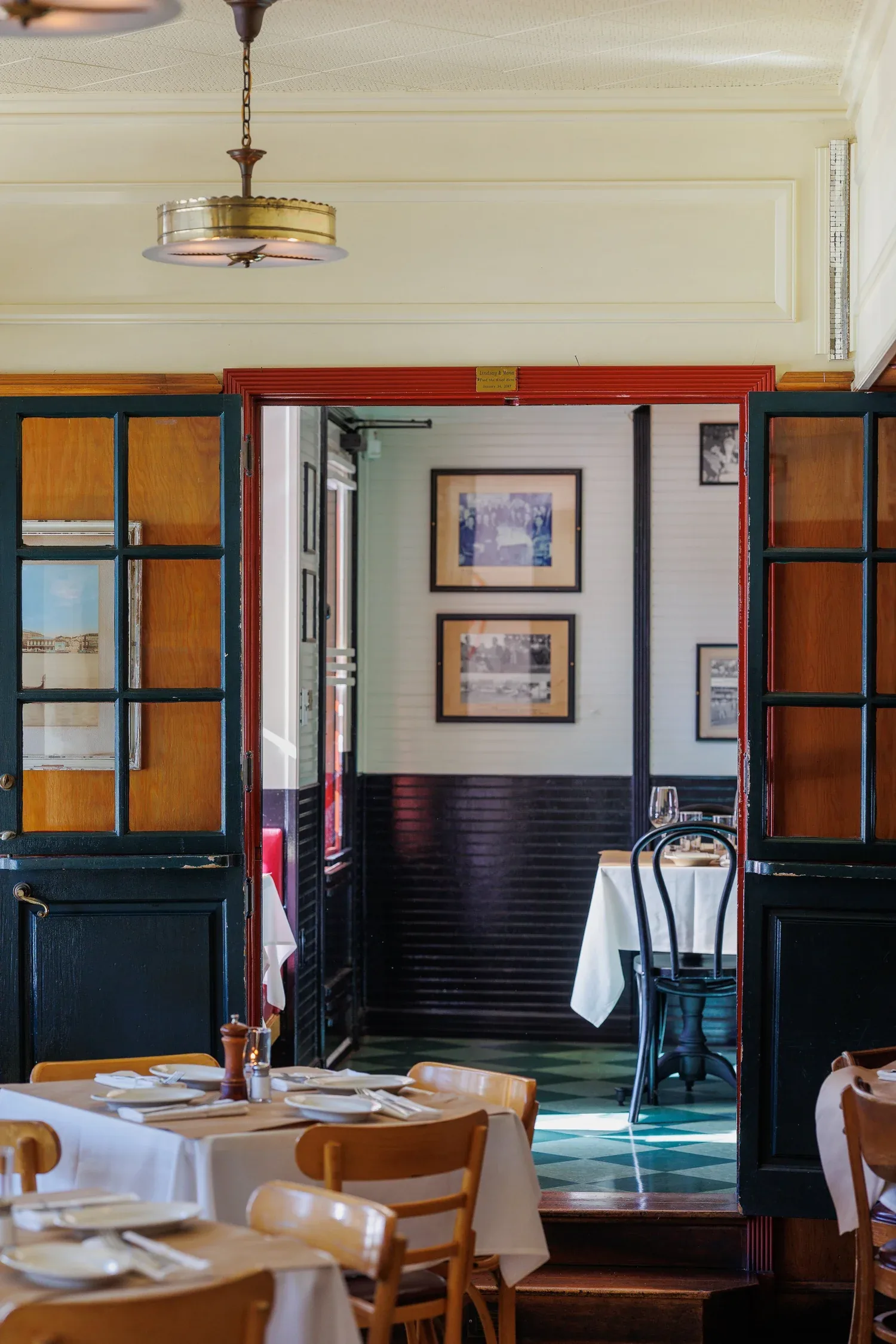 Elegant restaurant dining room with wood doors, vintage lighting, and formally set tables