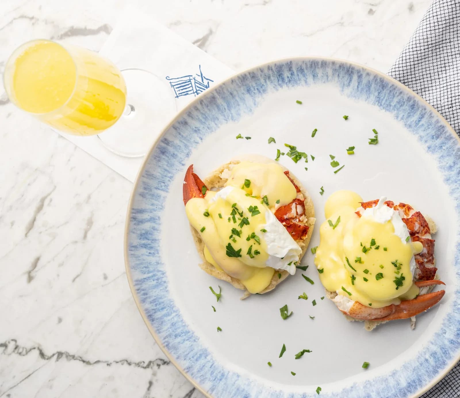 Lobster eggs Benedict with hollandaise and chives on blue-rimmed plate