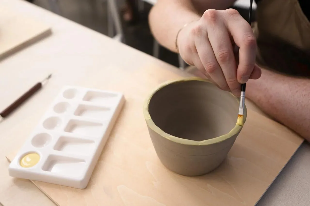 Potter painting glaze inside a ceramic bowl at a pottery studio workspace.