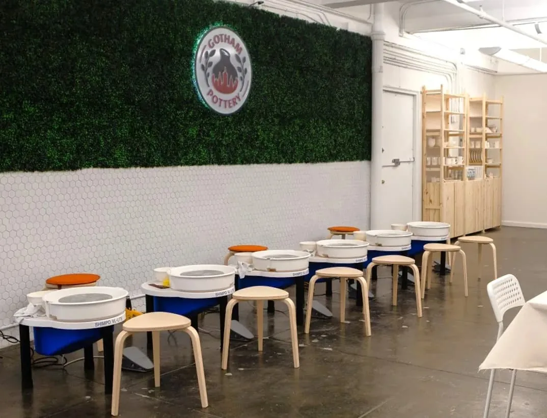 Pottery studio interior with multiple pottery wheels arranged in a row with orange seat cushions and wooden stools