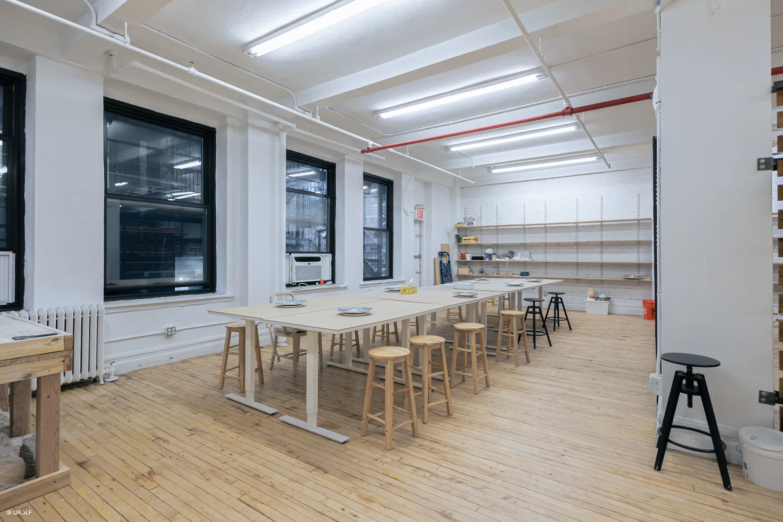 Bright pottery studio with wooden tables, bar stools, and open shelving