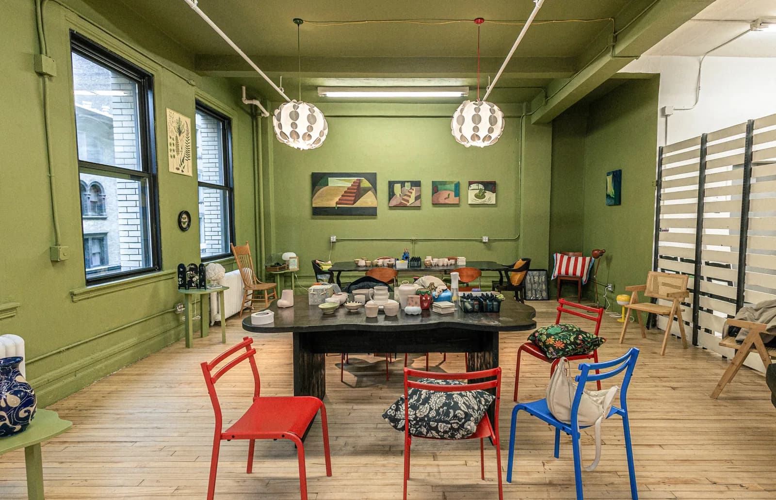 Pottery studio with green walls, central work table, red and blue chairs, and ceramic displays