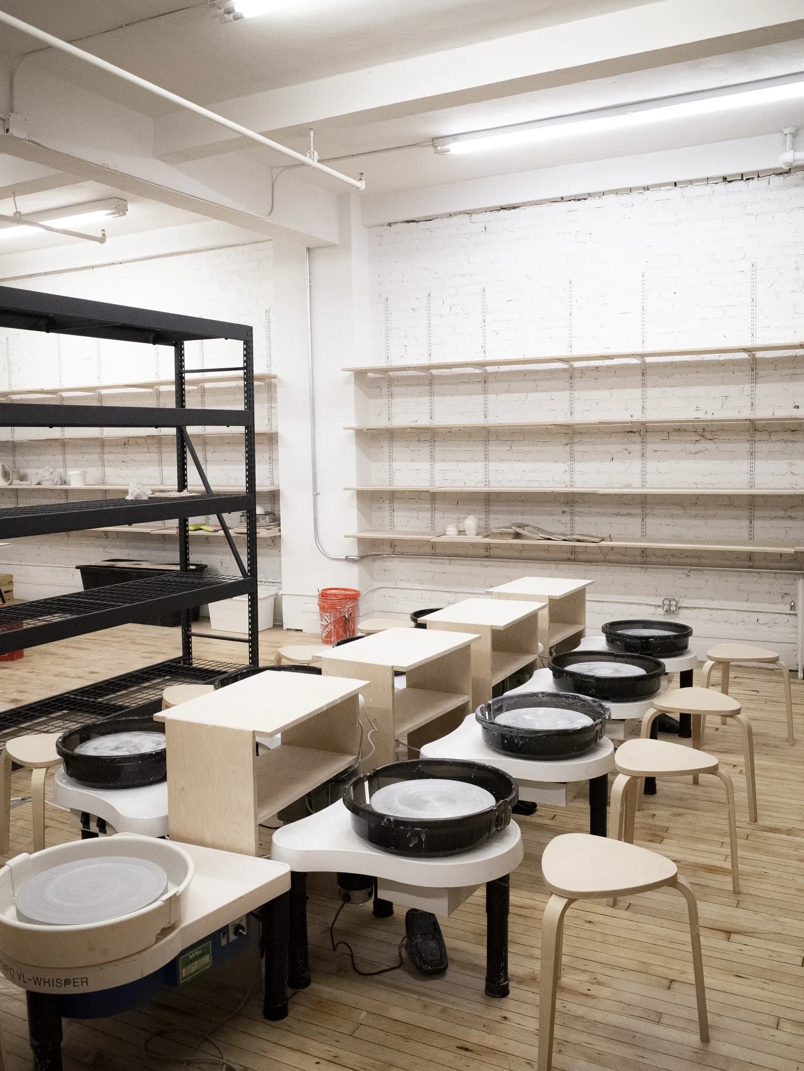 Pottery studio with ceramic wheels, wooden stools, and storage shelves along white walls