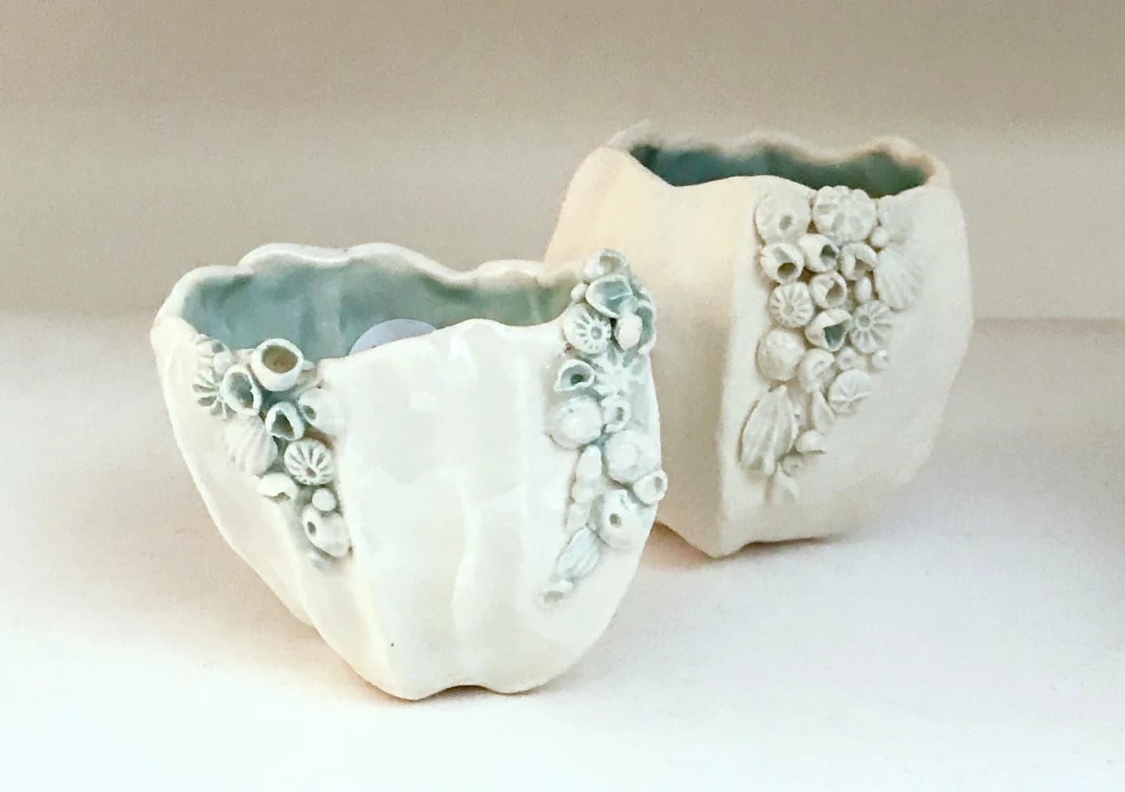 Two white ceramic vessels with shell and flower relief decorations and blue-glazed interiors