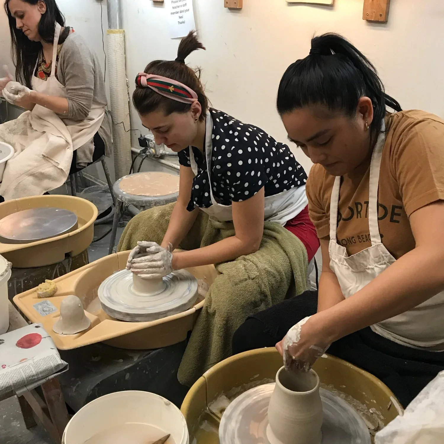 Pottery students work at wheels, shaping clay under instruction in a studio