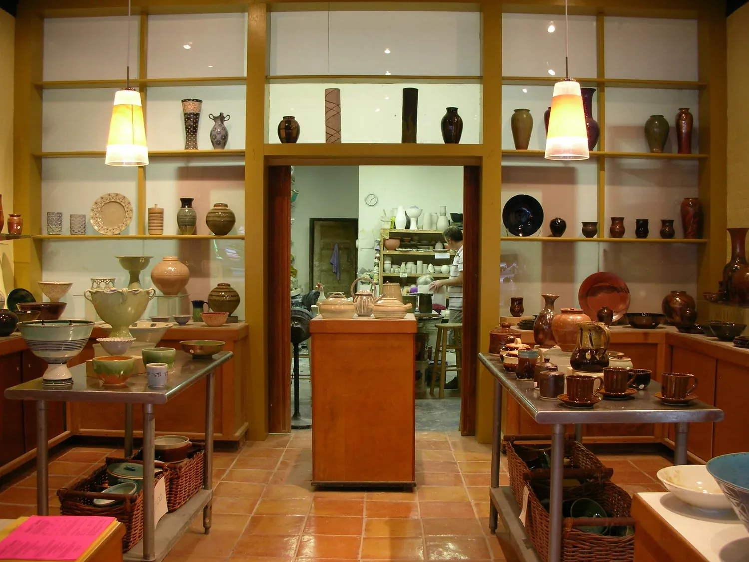Pottery showroom with handcrafted ceramic vessels displayed on wooden shelves and work tables