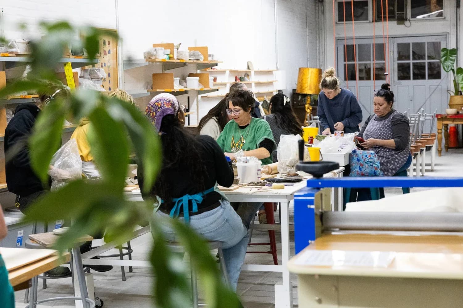 Pottery studio with people working at tables surrounded by ceramic pieces and shelving