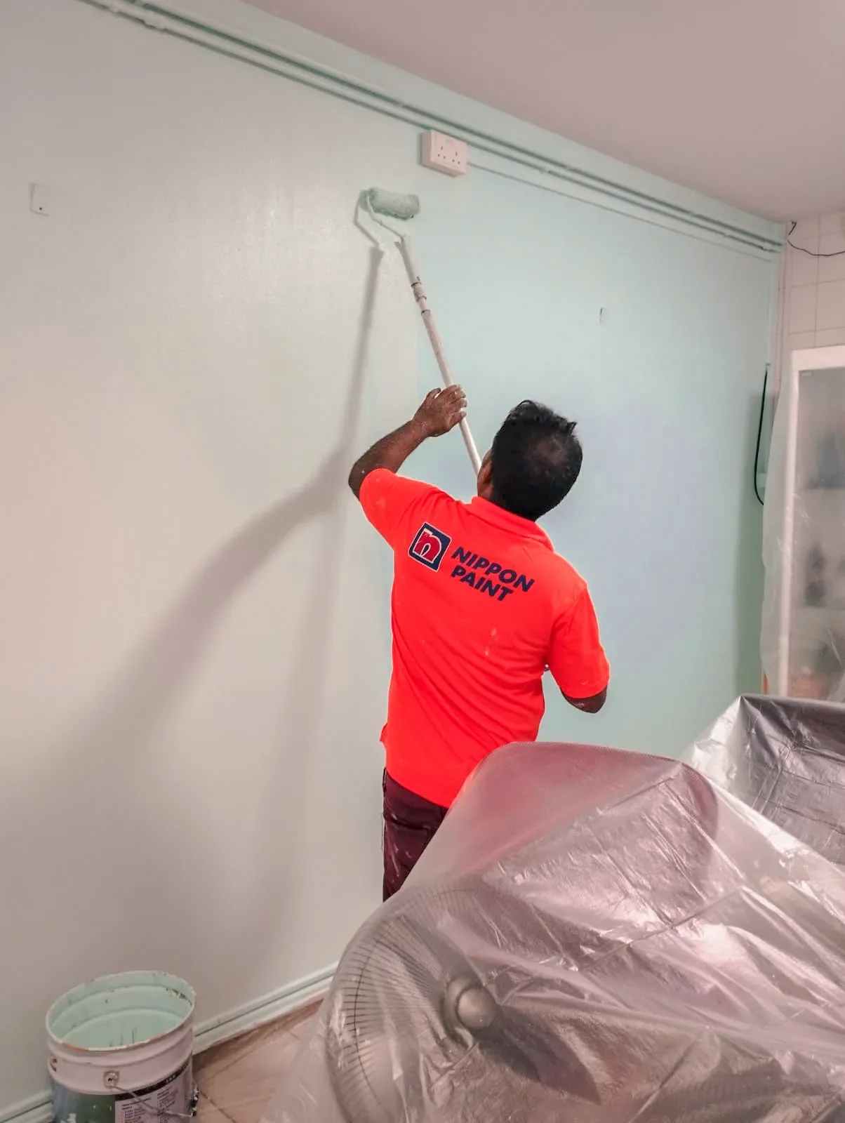 Painter in red shirt rolling white paint on interior wall