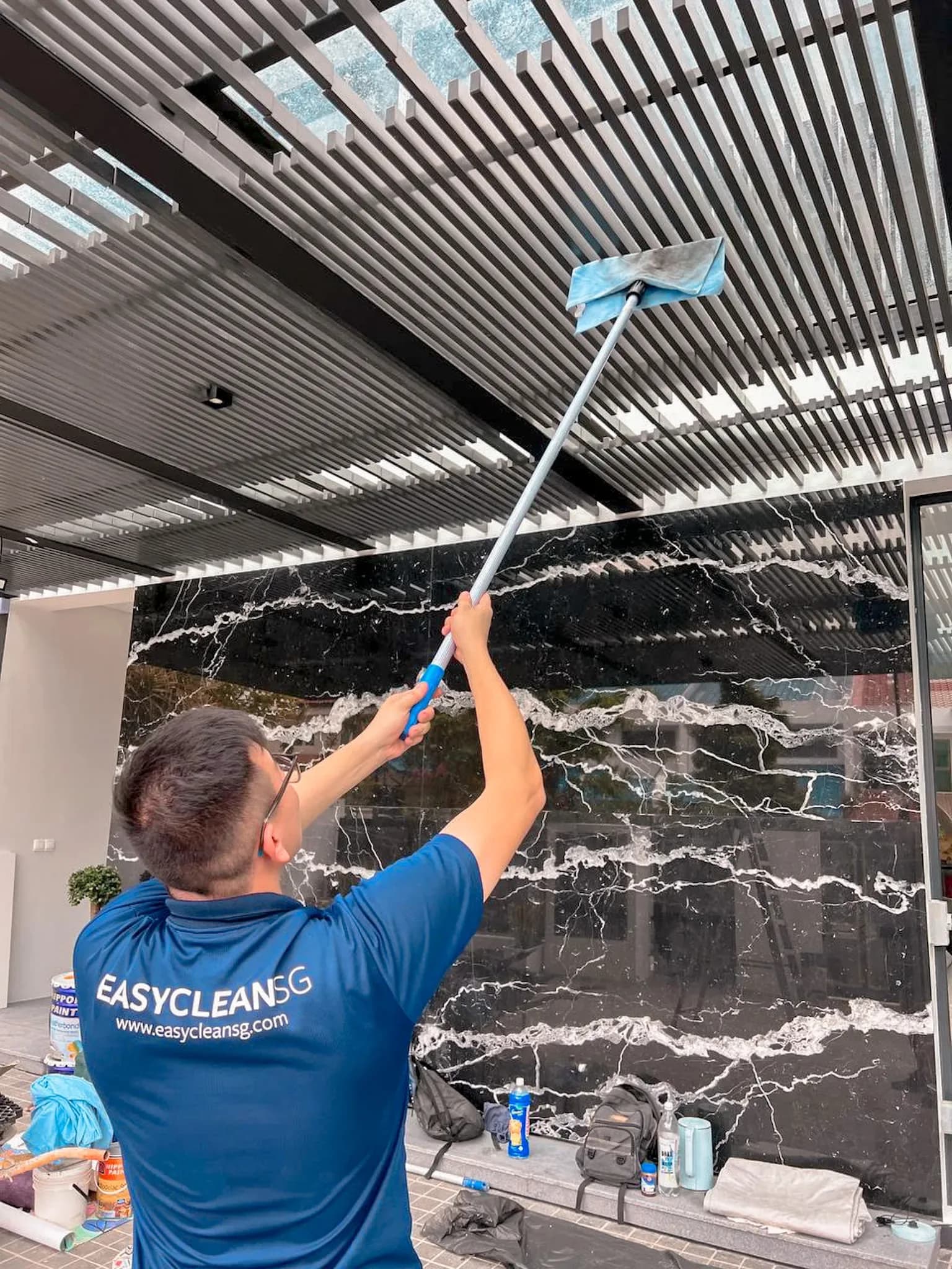 Worker in blue EASYCLEAN SG uniform cleaning a black marble-patterned glass panel with squeegee
