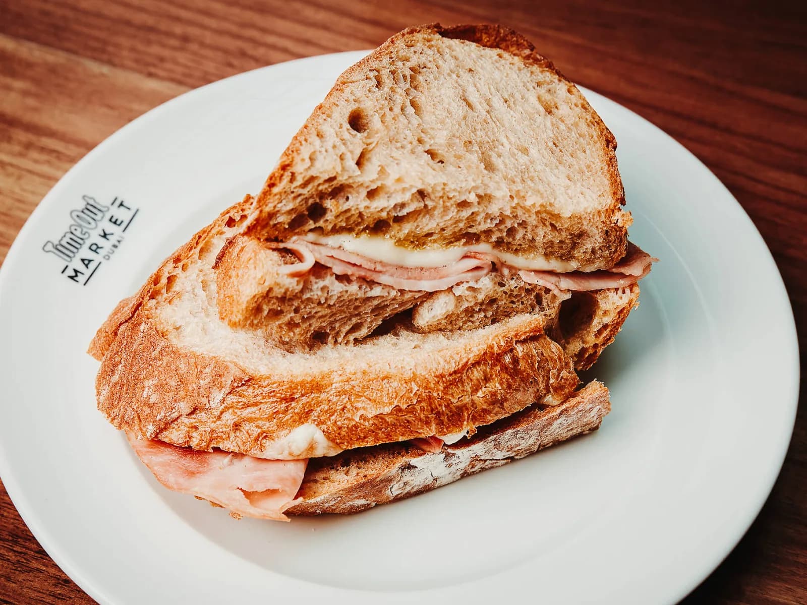 Toasted ham and cheese sandwich on white plate with Time Out Market branding