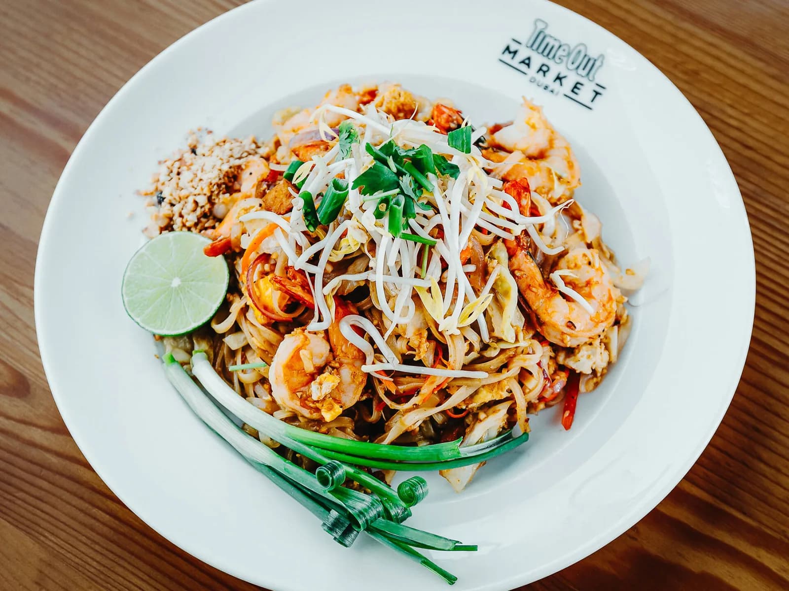 Pad thai with shrimp, garnished with fresh herbs and lime on a branded white plate