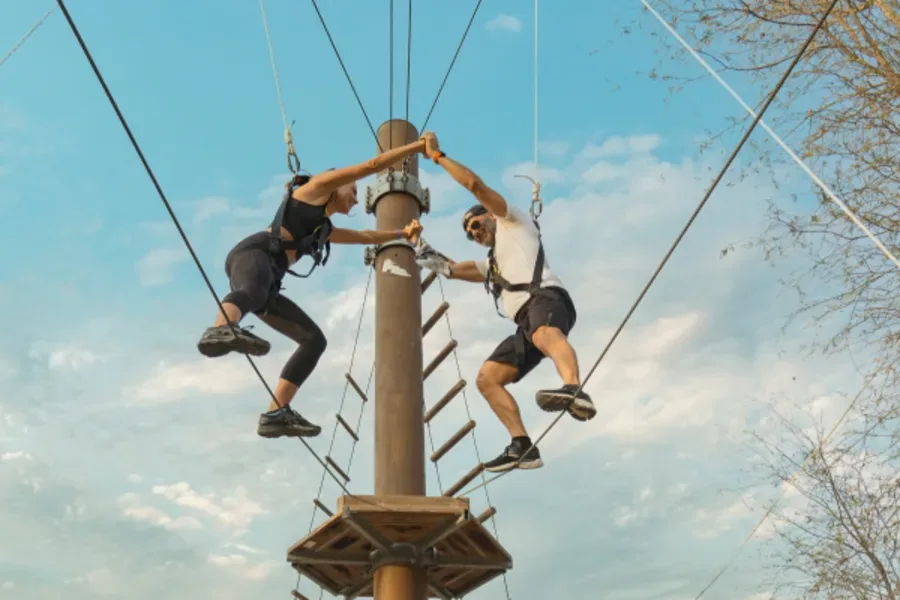 Two people on a high ropes course climbing wooden structures on a tall pole