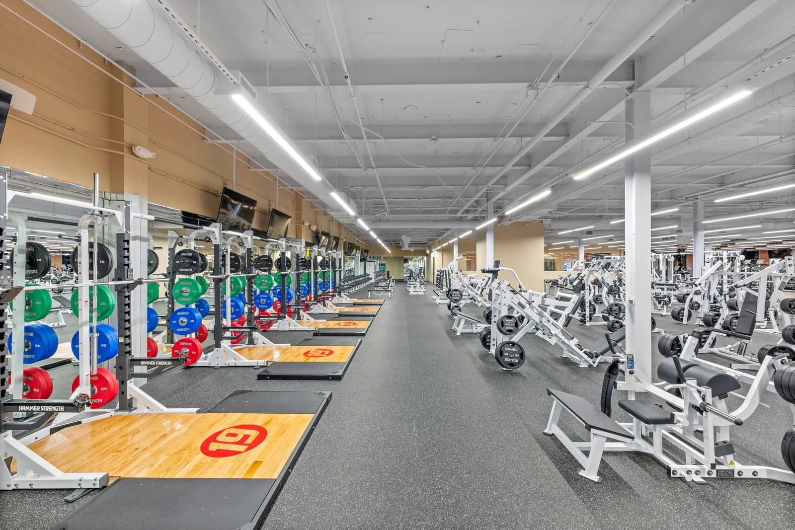 Gym floor with cardio machines, weight racks, and exercise equipment under bright ceiling lights