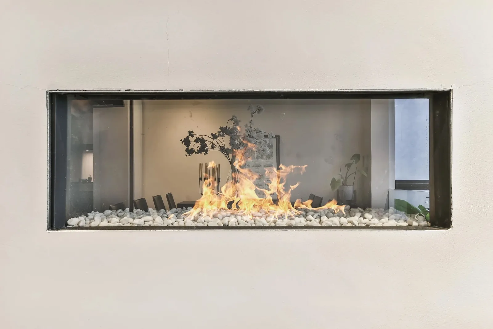 Linear fireplace insert with bright flames and white stone base, featuring decorative dried flowers