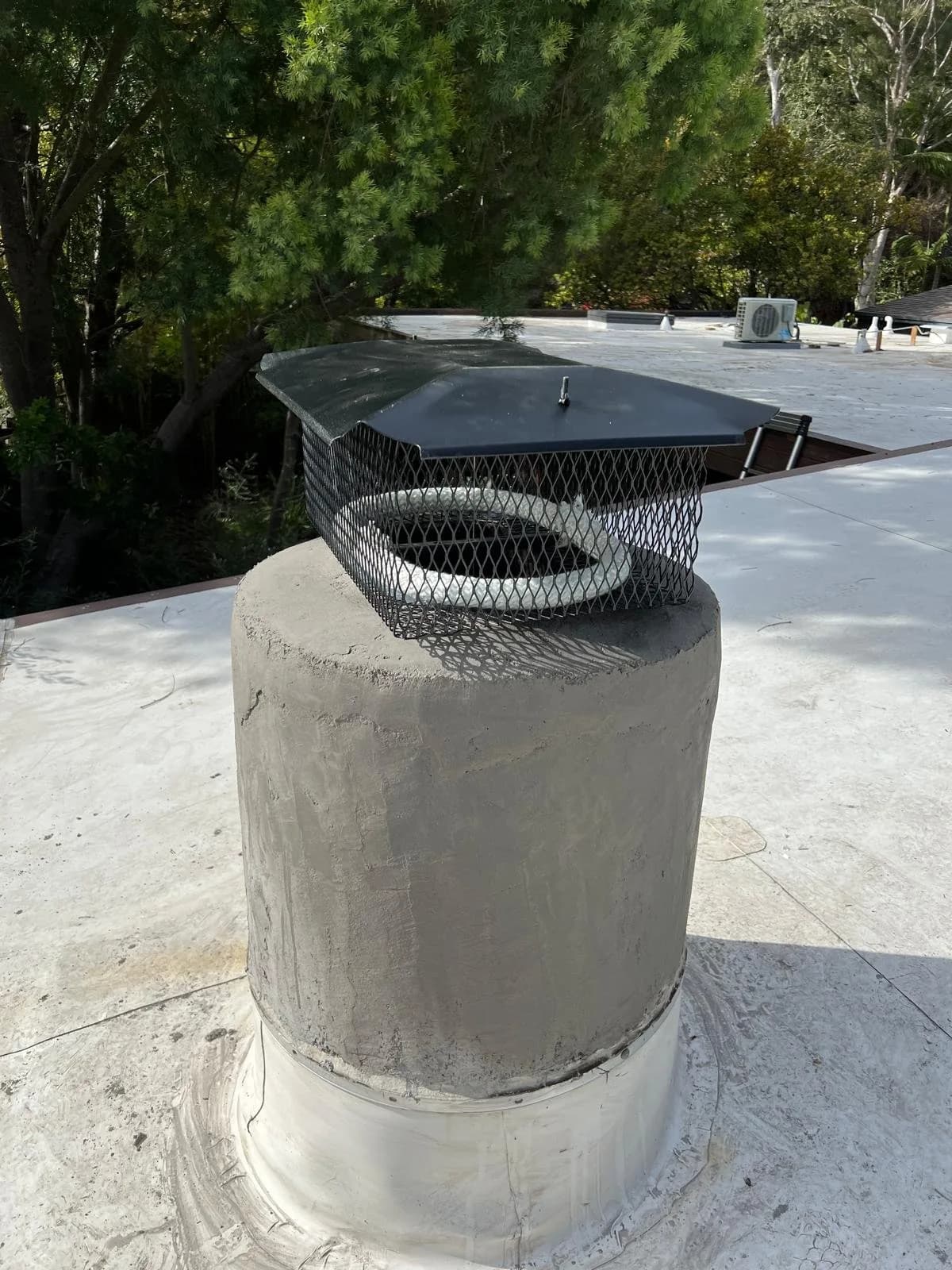 Chimney cap with mesh screening installed on concrete pipe on residential roof