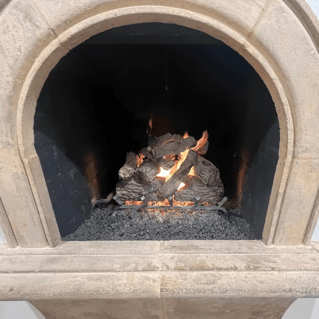 Fireplace with burning logs and flames inside a rounded stone chimney opening.