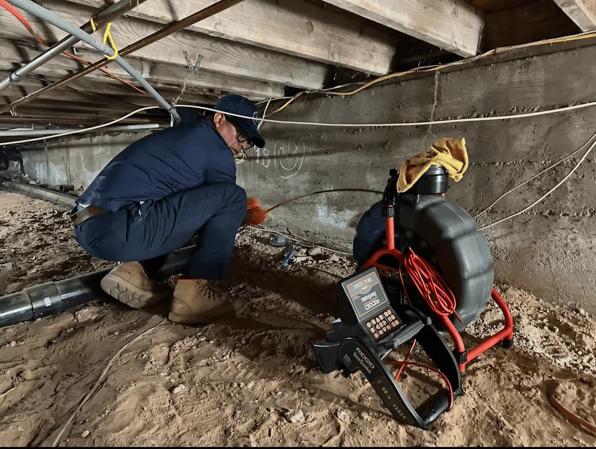 Plumber working on underground plumbing system with diagnostic equipment under concrete structure