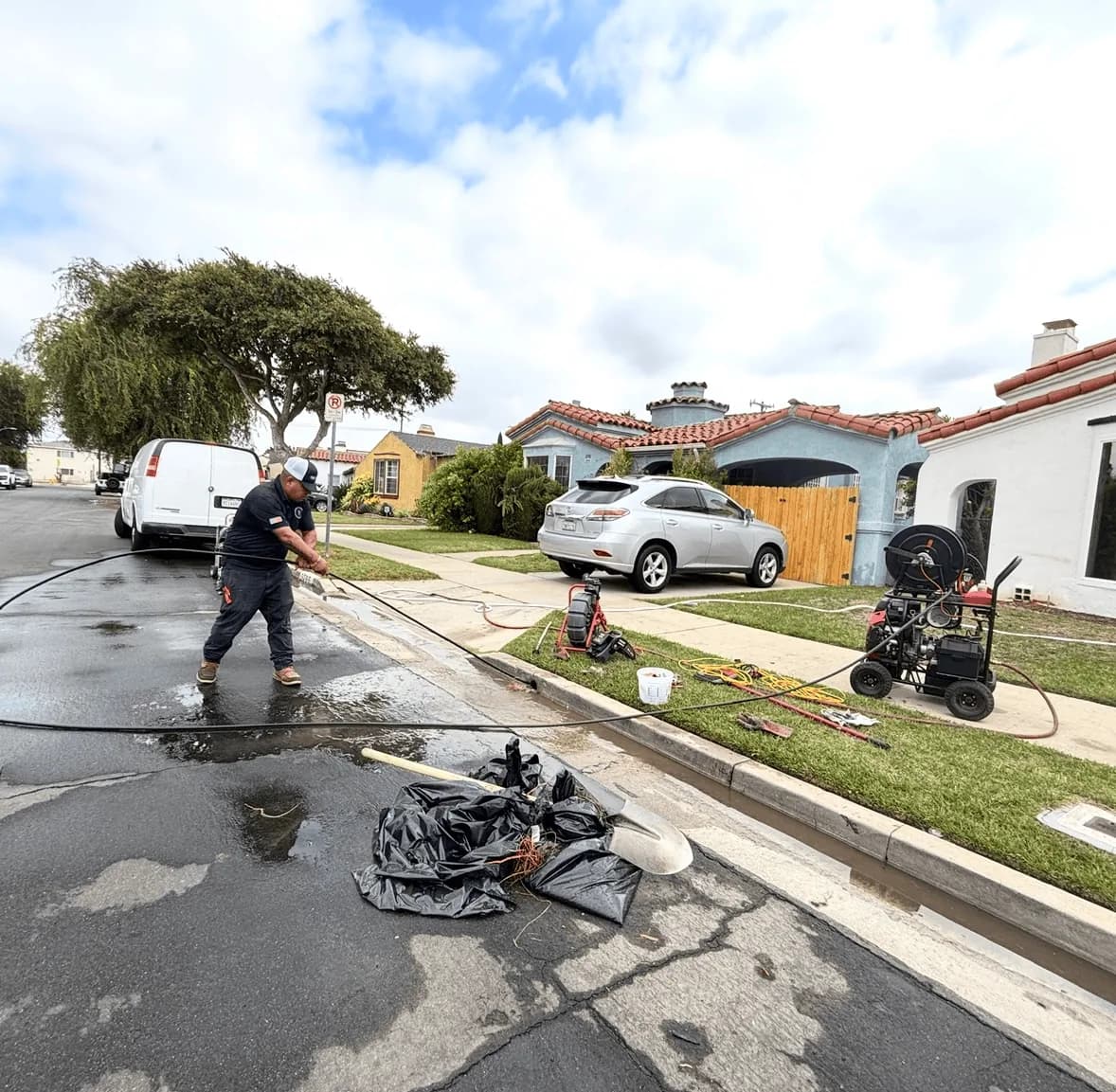 Plumber using drain cleaning equipment and hose on residential street with houses in background