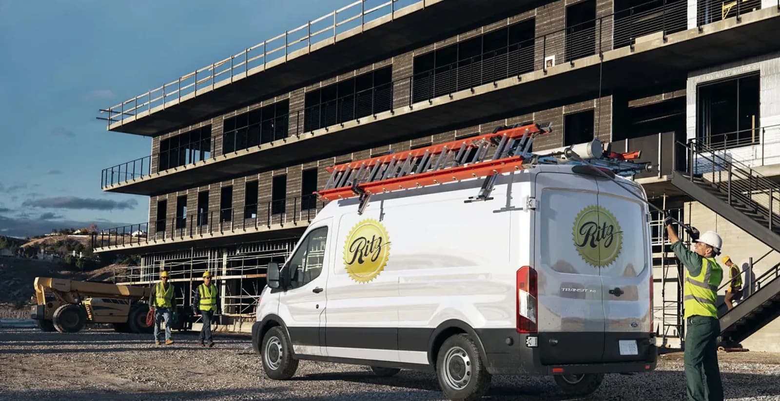 Ritz Plumbing service van at commercial construction site with workers and building