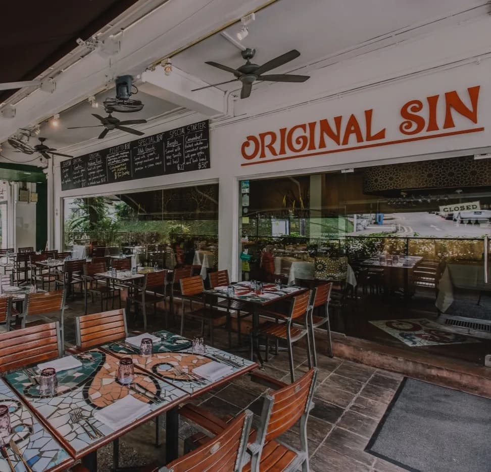 Original Sin restaurant dining area with wooden tables, orange chairs, and large signage